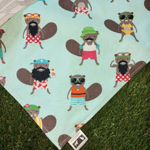 Load image into Gallery viewer, A close up of a dog bandana made out of mint green fabric with Beavers dressed in colourful bathing suits all over it laying on artificial turf.