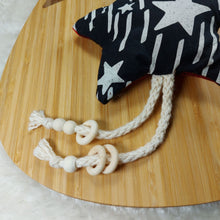 Load image into Gallery viewer, Close up of a cat toy made out of black and white star fabric and shaped like a star. It has natural cotton rope and wooden beads attached to them and is laying on a wooden board which is on a white fuzzy mat.