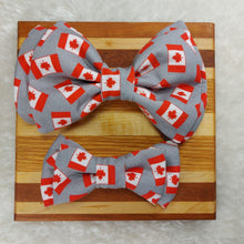 Load image into Gallery viewer, One large and one smaller dog bowtie made out of Canadian flag fabric laying on piece of wood, on white background.