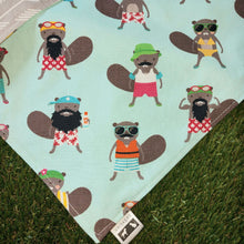 Load image into Gallery viewer, A close up of a dog bandana made out of mint green fabric with Beavers dressed in colourful bathing suits all over it laying on artificial turf.
