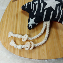 Load image into Gallery viewer, Close up of a cat toy made out of black and white star fabric and shaped like a star. It has natural cotton rope and wooden beads attached to them and is laying on a wooden board which is on a white fuzzy mat. 
