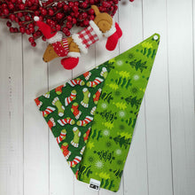 Load image into Gallery viewer, Dog Bandana made out of fabric with green and red Christmas stockings on it laying flat on a white background with a stuffed toy dog leaning against an artificial red wreath.
