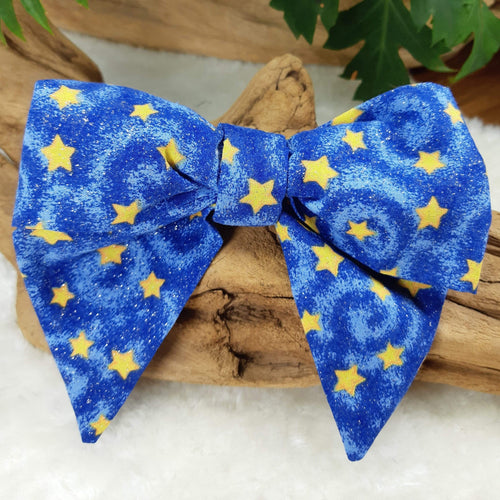 Stars Collar Bow. Help your pup put their best paw forward by wearing one of these pretty bows on their collar. Worn to the side, up front or at the back, its versatility makes dressing up an everyday possibility! This collar bow is suitable as a cat collar and a dog collar.  Measures 5.5” at its widest point. Made from 100% cotton fabric in a variety of patterns. Fastens to collars up to 1” wide. Elastic and snap fastener. Wiggles and Whiskers Canada Pet Accessories.