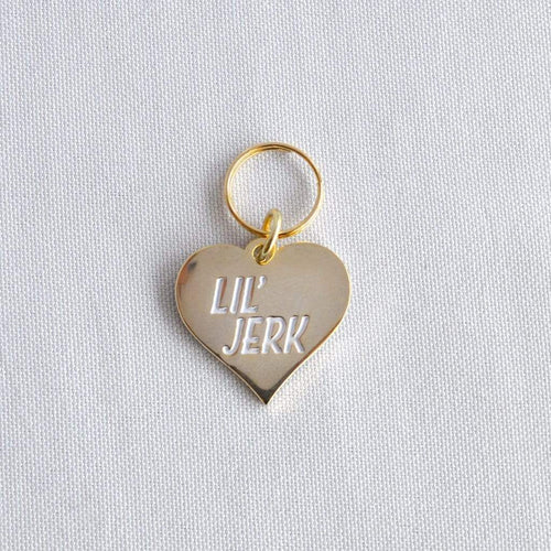 Gold Plated L'il Jerk Pet Tag. We all love our pets, but they can be little jerks sometimes too. So, in that spirit, Canadian company Boldfaced Goods created this charm to adorn the collars of our favorite pets.  Shiny backing perfect for engraving their name/number. Can also be worn as a pendant necklace for humans. Gold plated zinc alloy. Wiggles and Whiskers Canada Pet Accessories.